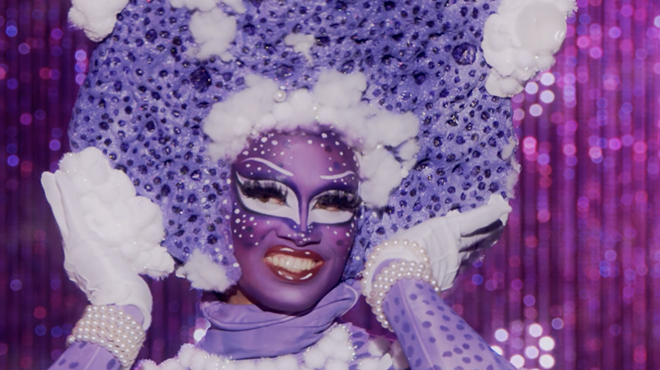 A drag queen in a purple outfit and face paint.
